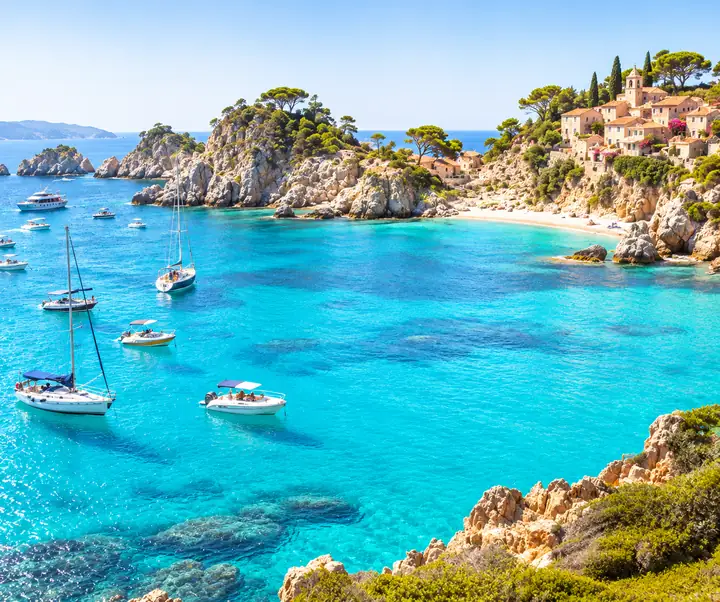 A sunlit coastal landscape with boats on turquoise water.
